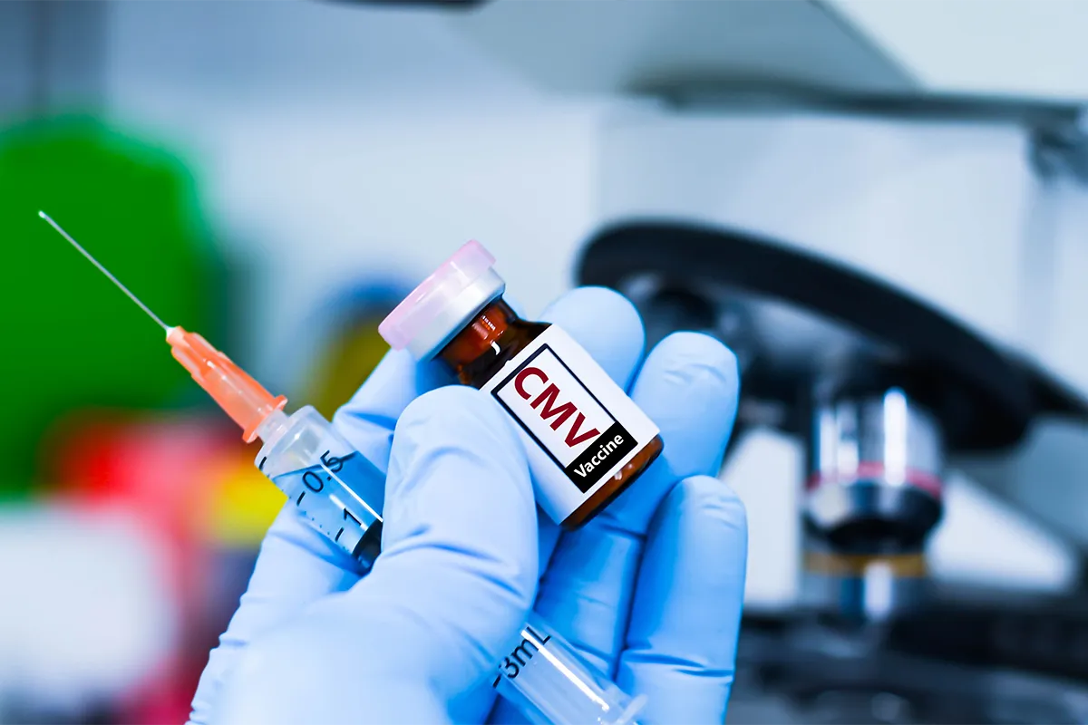 Flacon de vaccin CMV et seringue tenus par une main gantée.