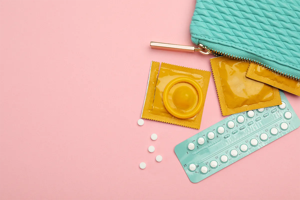 Pilule contraceptive et préservatifs posés près d’une pochette.